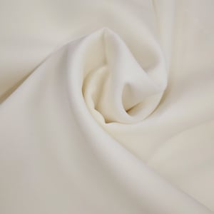 May include: A close-up shot of a cream-coloured fabric with gentle folds and shadows. The fabric has a smooth appearance and drapes softly, indicating a lightweight material. The overall aesthetic is neutral and elegant, ideal for clothing or home furnishings.