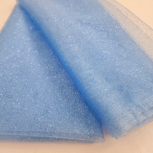 May include: A close-up of a light blue tulle fabric with sparkling glitter. The fabric is folded over itself, creating layers. The tulle has a fine mesh texture and is ideal for crafting, decorations, or apparel.