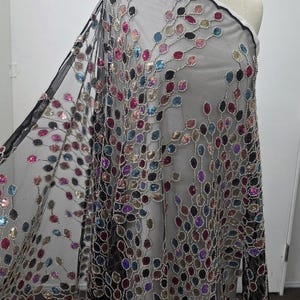 May include: Black sheer fabric with colorful sequin embellishments. The sequins are in various colors, including red, blue, purple, and gold, arranged in a floral pattern. The fabric is draped over a mannequin.