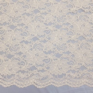 May include: Ivory white lace fabric with a delicate floral pattern. The lace has a scalloped edge.