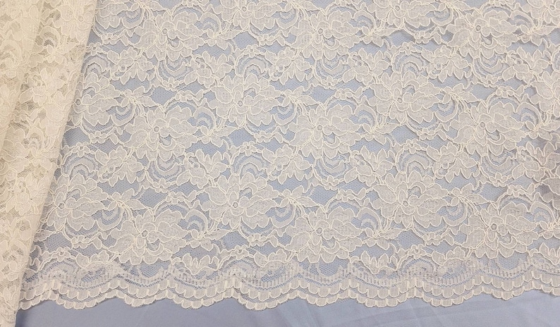 May include: Ivory white lace fabric with a delicate floral pattern. The lace has a scalloped edge.
