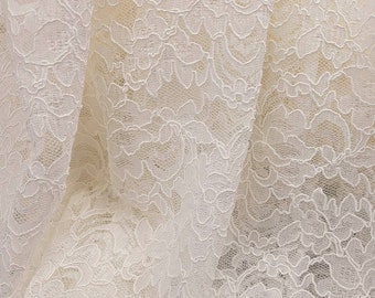 May include: White lace fabric with a delicate floral pattern. The lace is soft and flowing, with a subtle sheen.