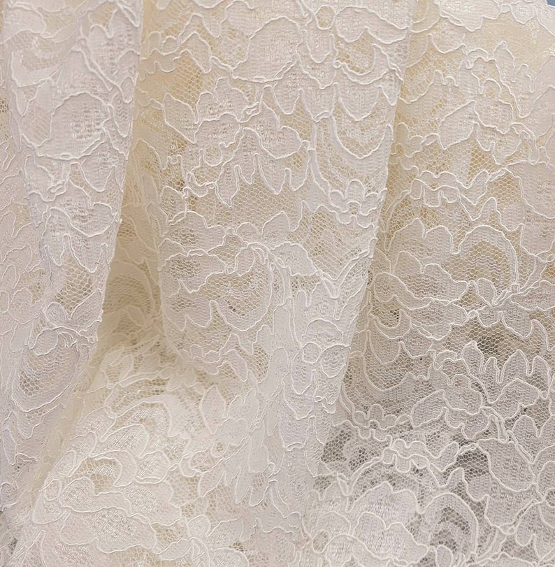 May include: White lace fabric with a delicate floral pattern. The lace is soft and flowing, with a subtle sheen.