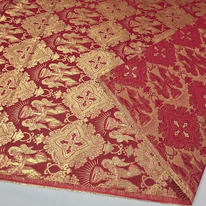 May include: Red and gold brocade fabric with a repeating pattern of ornate squares, angels, and crosses. The fabric has a luxurious sheen and a detailed design, suitable for decorative or liturgical purposes.