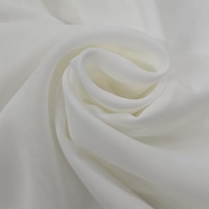 Puede incluir: Primer plano de una tela blanca con una textura suave y fluida. La tela está dispuesta en pliegues y curvas suaves, creando una sensación de movimiento y profundidad. El material parece ligero y delicado, con sutiles variaciones tonales.
