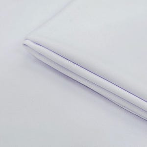 Può includere: Primo piano di un tessuto bianco piegato. Il tessuto appare liscio e morbido, con una sottile trama visibile. Le pieghe creano ombre, aggiungendo profondità all'immagine. L'impressione generale è di un tessuto pulito e immacolato.