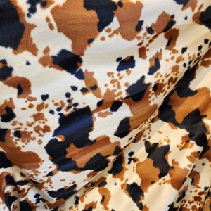 May include: A close-up of a white, brown, and black patterned fabric with a fuzzy texture. The fabric has a cowhide print.
