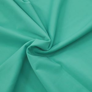Pode incluir: Um close-up de um tecido dobrado em uma cor turquesa vibrante. O tecido tem uma textura suave e parece ser um material leve, com dobras suaves e sombras que adicionam profundidade à imagem. A impressão geral é de um têxtil.