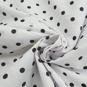 May include: White fabric with a pattern of evenly spaced black polka dots. The fabric is gathered and folded, creating soft shadows and texture. The polka dots are circular and of a consistent size, offering a classic and playful design.