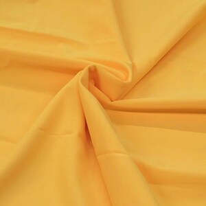 Pode incluir: Um tecido amarelo liso com uma textura macia e fluida. O tecido está dobrado e disposto de forma a mostrar sua textura e cor.