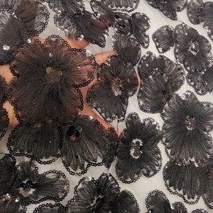 Puede incluir: Tela de encaje floral negra con lentejuelas. La tela presenta un patrón repetitivo de grandes flores en 3D.