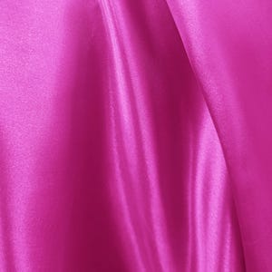 May include: Close-up of a vibrant fuchsia fabric with a smooth, satin-like texture. The fabric is draped, creating soft folds and highlights that catch the light. The color is a rich, saturated pink.
