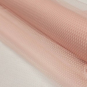 Puede incluir: Un rollo de tul de color rosa pálido con un sutil patrón de puntos. El tul es transparente y delicado, perfecto para manualidades y decoración.