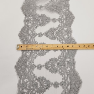 May include: Silver lace trim with a delicate floral pattern. The lace is approximately 2.5 cm wide.