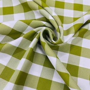 May include: Close-up of a fabric with a green and white checkered pattern. The fabric is folded, creating shadows and highlighting the texture. The pattern is a classic gingham design, suitable for various home decor projects.