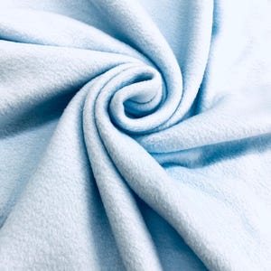 Può includere: Primo piano di un tessuto azzurro con una consistenza morbida e soffice. Il tessuto è disposto a spirale, creando un motivo a vortice. Il colore è un azzurro pallido e pastello, e il tessuto sembra essere di peluche.