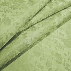 Könnte beinhalten: Nahaufnahme eines gefalteten, hellgrünen Stoffes mit einem floralen Rosenmuster. Der Stoff hat einen subtilen Glanz und eine strukturierte Oberfläche. Die Worte "Daylin Fabrics" sind unten rechts in Weiß gedruckt.