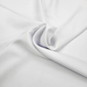 May include: White fabric with soft folds and wrinkles. The fabric is smooth and has a silky texture.