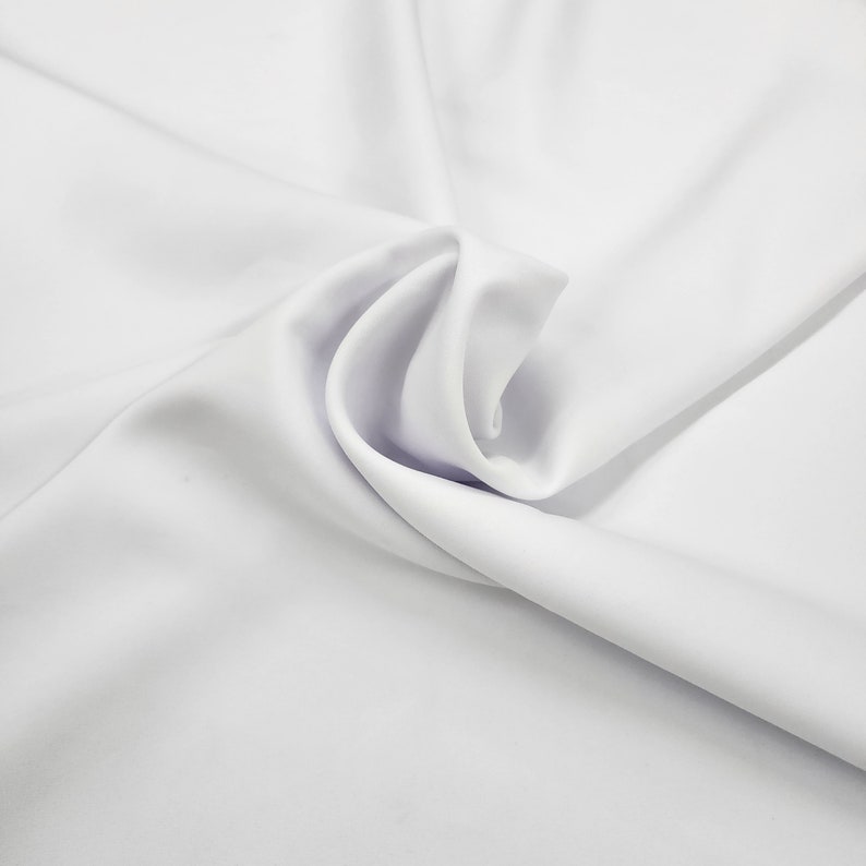May include: White fabric with soft folds and wrinkles. The fabric is smooth and has a silky texture.