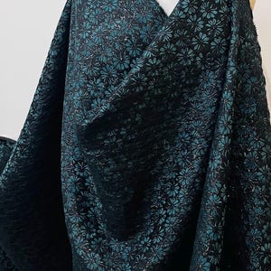 May include: Black fabric with a teal floral pattern. The fabric has a subtle shimmer and a textured surface.