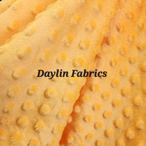 May include: Close-up of a yellow minky fabric with a textured dot pattern. The fabric is soft and plush, perfect for blankets, baby clothes, and other crafts. The text "Daylin Fabrics" is visible in the image.