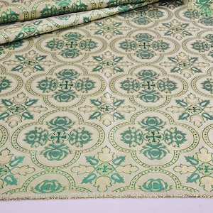 May include: Green and gold fabric with a repeating pattern of quatrefoils and crosses. The fabric has a subtle sheen and a textured surface.