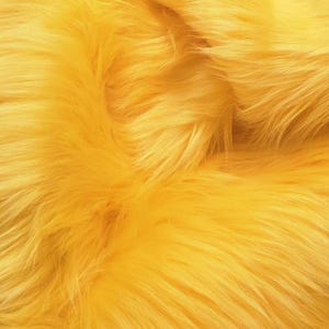 Puede incluir: Una tela de piel sintética de color amarillo vibrante con fibras largas, suaves y densas. El material presenta un tono amarillo dorado brillante y uniforme, con una textura peluda que crea pliegues y sombras naturales en la superficie.