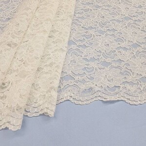 May include: White lace fabric with a delicate floral pattern. The lace has a scalloped edge.