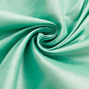 May include: Close-up of a swirl of mint green fabric. The fabric has a silky sheen and appears to be folded and draped, creating shadows and highlights. The texture is smooth and flowing, suggesting a lightweight material.