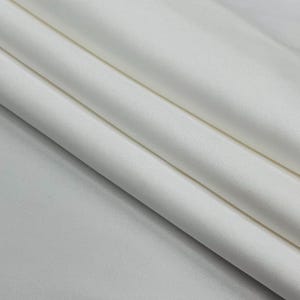 May include: Close-up of folded white fabric. The fabric has a smooth texture and is folded in soft, flowing lines. The folds create shadows and highlights, adding depth to the image. The fabric appears to be a solid color.