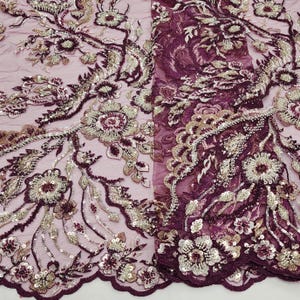 May include: Close-up of a burgundy lace fabric with intricate floral embroidery. The design features silver and gold metallic thread, sequins, and beads. The delicate pattern includes flowers, leaves, and vines, creating a luxurious and ornate textile.