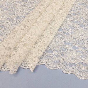 May include: White lace fabric with a delicate floral pattern. The lace has a scalloped edge.
