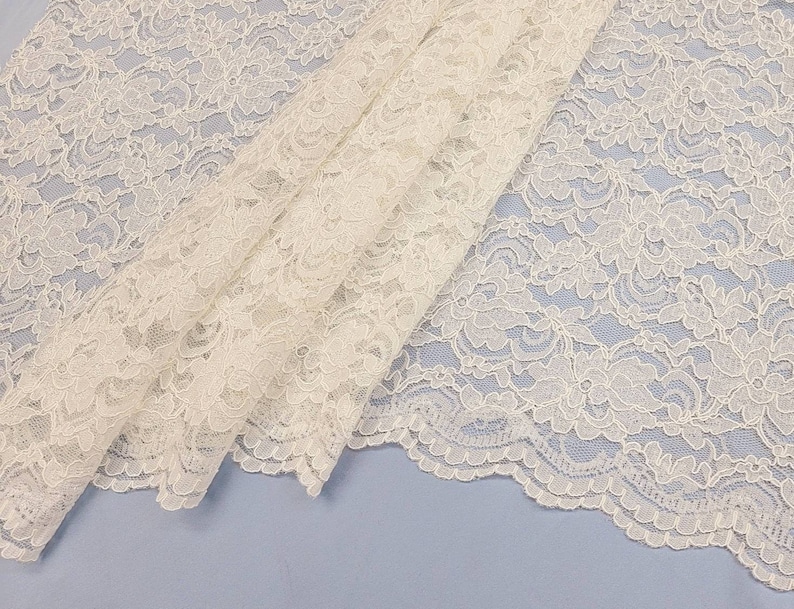 May include: White lace fabric with a delicate floral pattern. The lace has a scalloped edge.
