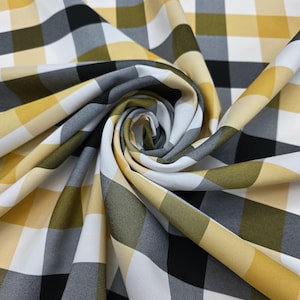 Puede incluir: Primer plano de una tela con un patrón de cuadros grandes. El patrón presenta cuadrados en negro, blanco, amarillo y gris. La tela está doblada y arremolinada, mostrando los diferentes colores y texturas del material.