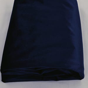 May include: A folded piece of navy blue velvet fabric. The fabric is a deep, rich shade of blue, and the folds create shadows that highlight the texture of the material. The fabric appears soft and luxurious.
