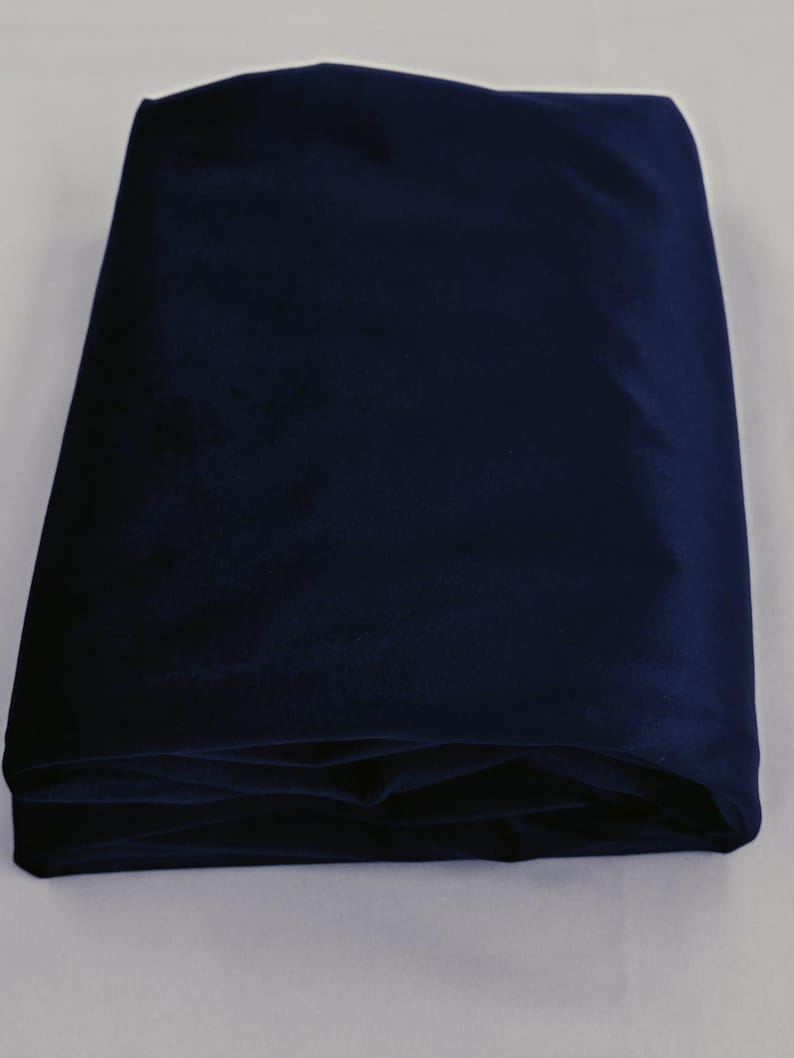 May include: A folded piece of navy blue velvet fabric. The fabric is a deep, rich shade of blue, and the folds create shadows that highlight the texture of the material. The fabric appears soft and luxurious.