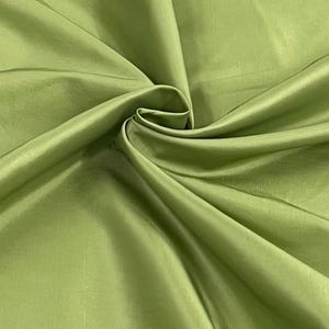 Puede incluir: Primer plano de una vibrante tela verde lima con un brillo sedoso. El material está recogido y doblado, creando suaves sombras y reflejos. La tela parece suave y lujosa, lo que sugiere que podría usarse para ropa o decoración del hogar.