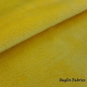 May include: A close-up of a bright yellow fabric with a soft, fuzzy texture. The fabric is folded in half, showing the pile on both sides.