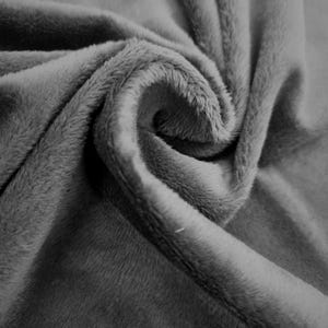 Puede incluir: Una tela suave y afelpada de color gris medio sólido. El material presenta una textura densa de pelo corto que crea sombras y reflejos sutiles dentro de los pliegues, mostrando la superficie lisa y aterciopelada del material textil.
