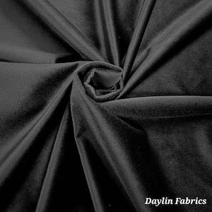 May include: Close-up of a black velvet fabric, showing its soft texture and smooth surface. The fabric is draped and folded, highlighting its luxurious feel. Daylin Fabrics is printed in the bottom right corner.