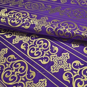 Pode incluir: Close-up de um tecido roxo com padrões dourados ornamentados. O design apresenta motivos florais e de rolagem dourados repetidos, sobre um fundo roxo escuro. O tecido está dobrado, mostrando a textura e os detalhes do design.