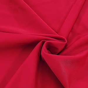 Könnte beinhalten: Nahaufnahme eines glatten, roten Stoffes. Der Stoff ist gefaltet und drapiert, wodurch seine Textur und Farbe sichtbar werden.