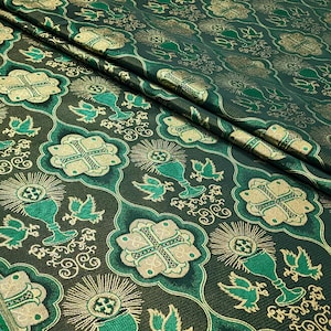 May include: Green fabric with a repeating pattern of gold chalices, crosses, and doves. The fabric has a woven texture.