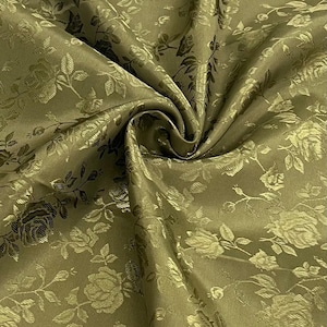 Pode incluir: Tecido verde-oliva com um padrão floral de rosas. O tecido está dobrado, mostrando a textura e o brilho do material. As rosas e folhas são em relevo, criando um contraste sutil. Ideal para costura e decoração.