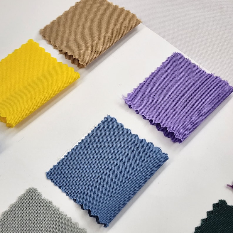 May include: Five fabric swatches in different colors: beige, yellow, purple, blue, and gray. The swatches are arranged in a row on a white surface.