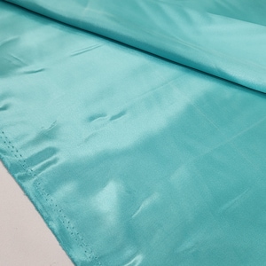 May include: A smooth, turquoise fabric with a subtle sheen. The fabric is folded in half, showing the texture and color.