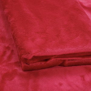 May include: Close-up of a deep red plush fabric. The fabric is soft and fuzzy, with a slight sheen. Daylin Fabrics is printed in white at the bottom of the image.
