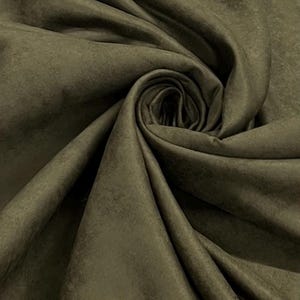 May include: Close-up of olive green fabric with a textured, suede-like appearance. The material is draped and folded, creating a swirling pattern with a central spiral. The fabric has a matte finish and a subtle color variation.