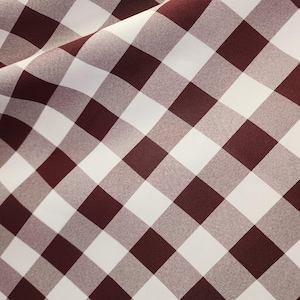 Op de afbeelding: Een close-up van een rood-witte gingham stof. De stof heeft een geruit patroon met rode vierkanten en witte vierkanten.