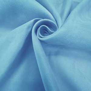 Può includere: Primo piano di un vortice di tessuto azzurro. Il materiale ha una consistenza morbida e vellutata ed è strettamente arrotolato al centro, creando un effetto a spirale. Il tessuto sembra essere di colore uniforme, con sottili variazioni di tono dovute alle pieghe.
